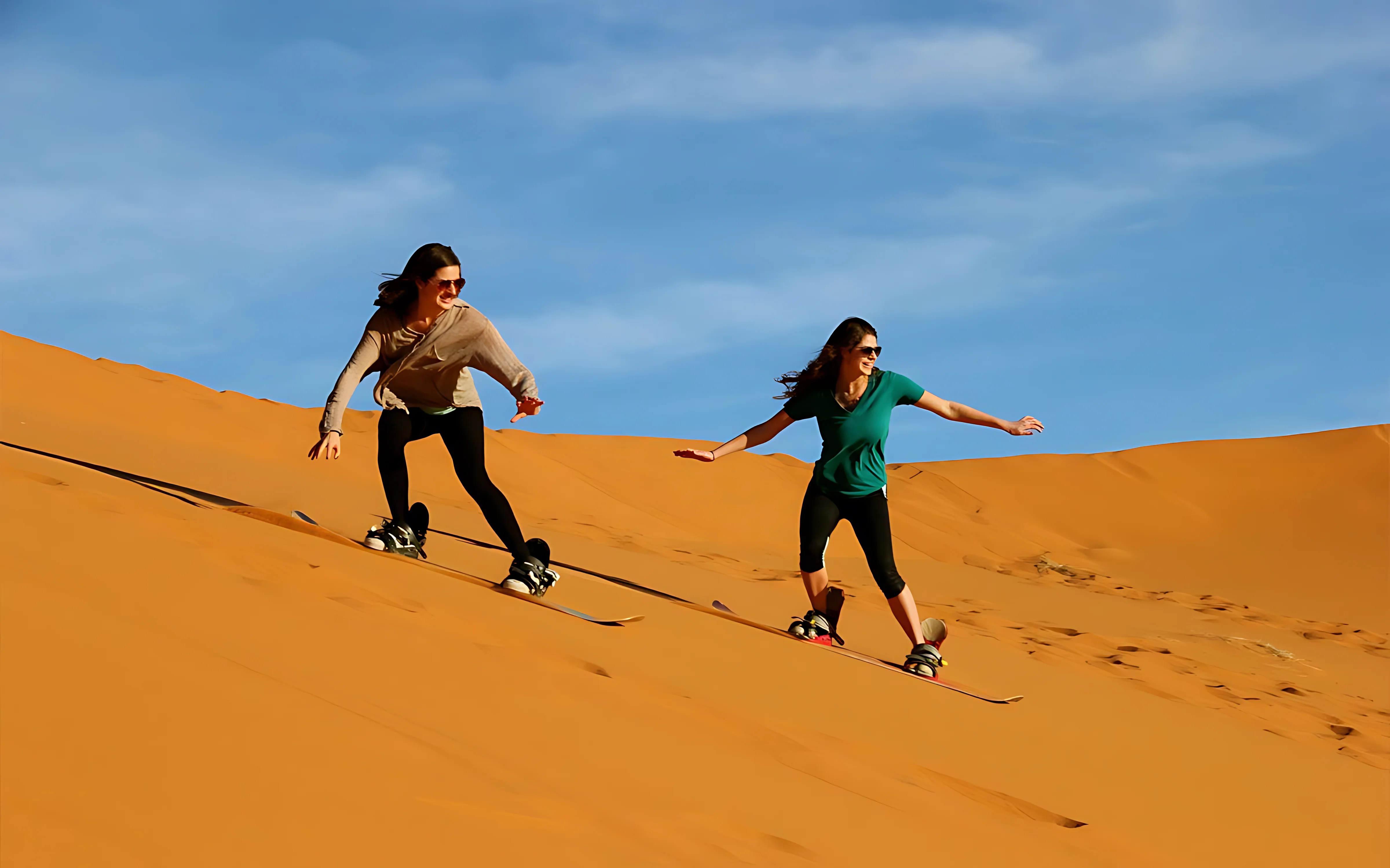 Women sandboarding down golden dunes during a Dubai desert safari